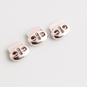 May include: Three metallic silver cord locks, oval-shaped with two holes and a rectangular top. These cord locks are designed to secure and adjust drawstrings or cords on various items.