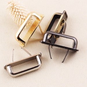 Könnte beinhalten: Drei D-Ring-Beschläge aus Metall in Gold, Silber und Schwarz. Die Ringe sind zum Anbringen an Taschen, Handtaschen oder anderen Lederwaren gedacht.