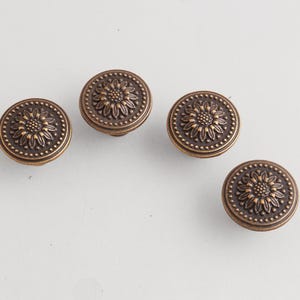 May include: Four antique bronze cabinet knobs with a sunflower design. Each knob is round with a raised floral center and a dotted border. The knobs are set against a white background.