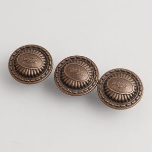 Pode incluir: Três puxadores de armário em bronze antigo. Cada puxador redondo apresenta um centro oval e uma borda externa decorativa. O centro de cada puxador tem um design de script ornamentado.