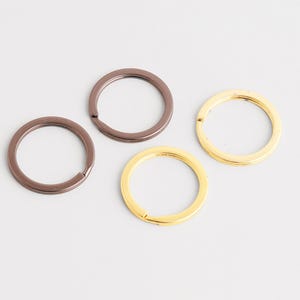 May include: Four metal key rings in shades of brown and gold. The key rings are circular with a split opening for attaching keys. The key rings are on a white background.
