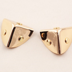 Può includere: Due protezioni per angoli in metallo color oro con bordi arrotondati e tre piccoli rivetti rotondi color oro.