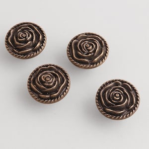 May include: Four bronze-colored rose-shaped cabinet knobs. Each knob features a detailed rose design in the center, surrounded by a rope-like border. The knobs are round and have a vintage aesthetic.