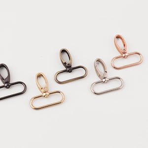 Può includere: Un assortimento di chiusure girevoli in metallo in varie finiture: nero, oro, bronzo, argento e oro rosa. Ogni chiusura ha una base ovale e un gancio girevole.