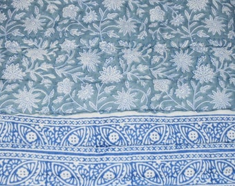 Op de afbeelding: Een blauwe en witte stof met een bloemenpatroon en een blauwe en witte rand. De stof heeft een gestikte textuur.