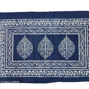 May include: A blue cotton fabric with a white pattern of leaves and floral designs. The fabric has a border with a repeating pattern.