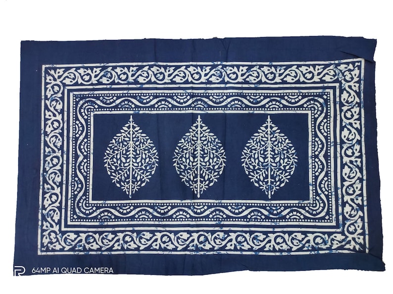 May include: A blue cotton fabric with a white pattern of leaves and floral designs. The fabric has a border with a repeating pattern.