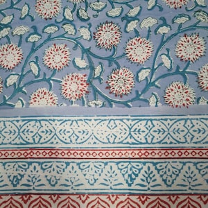 Op de afbeelding: Een blauwe en witte stof met een bloemenpatroon. De stof heeft een rand met een herhalend patroon van bladeren en bloemen.