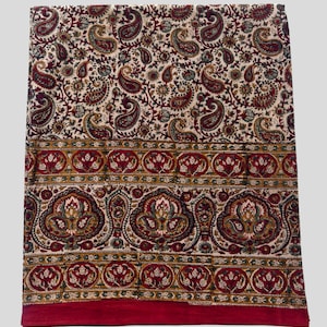Può includere: Un tessuto piegato con sfondo color crema e un motivo paisley ripetuto in bordeaux, verde e oro. Un ampio bordo bordeaux con disegni floreali ornati corre lungo il bordo inferiore. Il tessuto sembra essere di cotone.