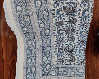 Op de afbeelding: Een wit katoenen dekbed met een blauwe en grijze bloemenprint. Het dekbed heeft een rand met een herhalend patroon van bladeren en bloemen.