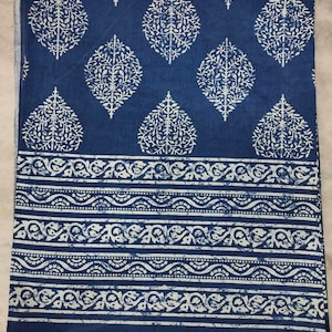 May include: A blue cotton fabric with a white floral pattern. The fabric has a border of white floral designs.