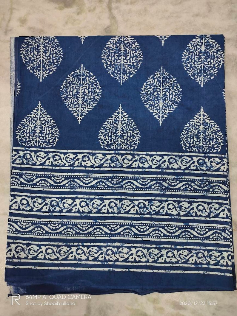 May include: A blue cotton fabric with a white floral pattern. The fabric has a border of white floral designs.