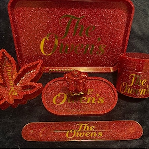 May include: Red glitter rolling tray set with gold lettering that says "The Owen's". The set includes a tray, a small jar, a leaf-shaped tray, a small round tray, and a long, thin tray.