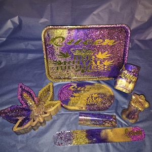 May include: A set of purple and gold glitter resin accessories including a rectangular tray with the text Queen Her Royal Highness, a leaf-shaped dish, an oval tray, a small jar, a torso-shaped figure, a cylindrical container, and a long stirrer.