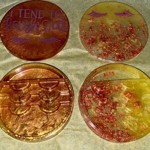 May include: Four round, clear resin trays with gold glitter and copper flakes. One tray has the text "I tend to lash out" with purple eyelashes. Another tray has three rows of eyelash holder compartments. The remaining two trays have a single compartment.
