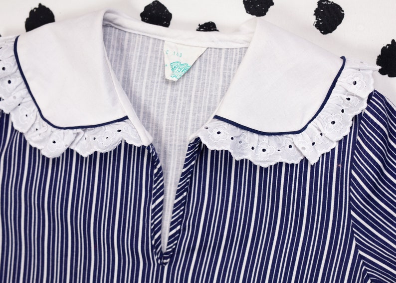 May include: A white collared shirt with a blue and white striped pattern and a white lace trim. The collar has a navy blue trim. The shirt has a small tag that says "C. Rae".