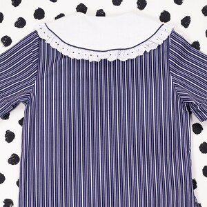 May include: A blue and white striped short-sleeved shirt with a white collar and a lace trim.