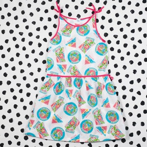 Puede incluir: Vestido blanco sin mangas con ribete rosa y un patrón de círculos azules y verdes con el texto "Keep the Pacific Islands Beautiful" y "Keep the Ocean Clean".
