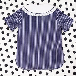 May include: A blue and white striped shirt with a white collar and a white lace trim. The shirt has short sleeves.