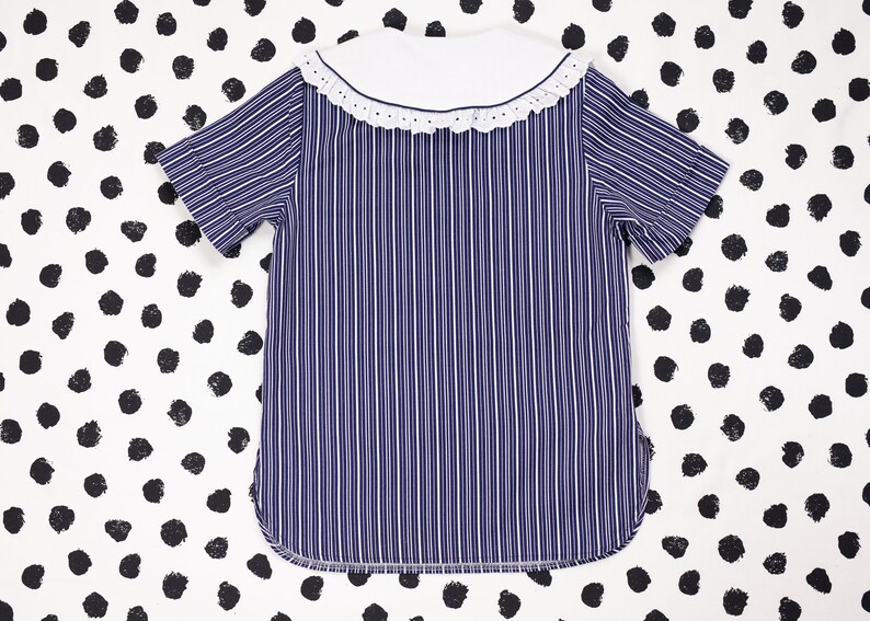 May include: A blue and white striped shirt with a white collar and a white lace trim. The shirt has short sleeves.