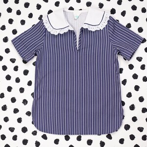 May include: A blue and white striped shirt with a white collar and lace trim. The shirt has short sleeves and a V-neck.