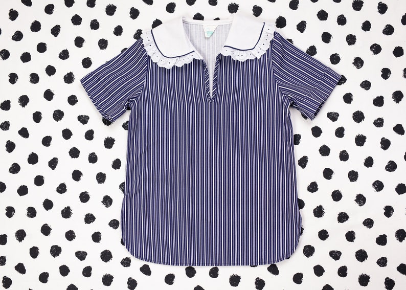May include: A blue and white striped shirt with a white collar and lace trim. The shirt has short sleeves and a V-neck.
