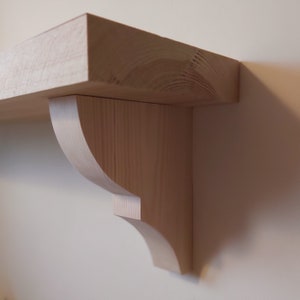 May include: A natural wood shelf with a curved bracket. The shelf is made of unfinished pine wood.
