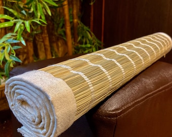 May include: A rolled up natural woven mat with a white fabric edging. The mat is resting on a brown leather surface.