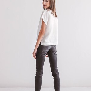 A white linen top with short sleeves and dark gray skinny jeans. The model is wearing black sandals. The outfit is simple and elegant, suitable for casual wear.