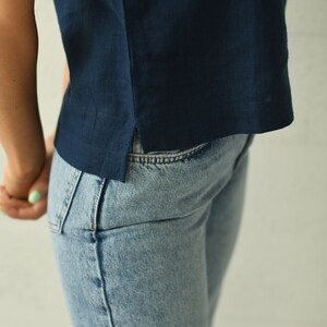 A close-up of a person wearing a navy blue linen top and light blue denim jeans. The top has a simple design with a side slit. The jeans are a classic style.