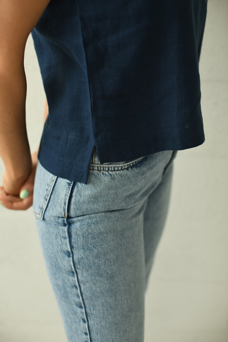 A close-up of a person wearing a navy blue linen top and light blue denim jeans. The top has a simple design with a side slit. The jeans are a classic style.