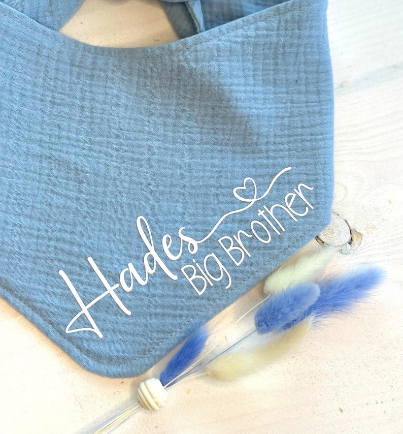 May include: A light blue bandana with the text "Hades Big Brother" in white cursive lettering and a small heart symbol.