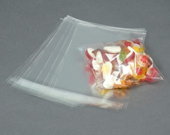 May include: A stack of clear plastic bags with a single bag filled with colorful candies, including red, white, orange, and yellow.