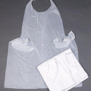 以下が含まれることがあります： 首紐と結び紐が付いた白いプラスチック製の使い捨てエプロン。エプロンは折り畳んでグレーの表面に平らに置かれています。