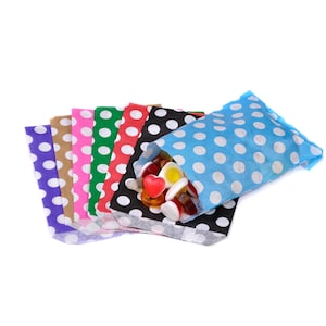 May include: A set of colourful polka dot paper bags with white dots. The bags are folded and arranged in a fan shape. The top bag is light blue and has a variety of colourful sweets inside.