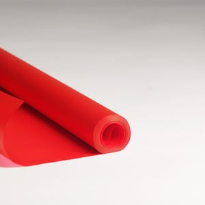 May include: A roll of bright red wrapping paper is partially unrolled, revealing the smooth, glossy surface. The paper is rolled tightly, creating a cylindrical shape.