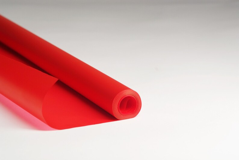 May include: A roll of bright red wrapping paper is partially unrolled, revealing the smooth, glossy surface. The paper is rolled tightly, creating a cylindrical shape.