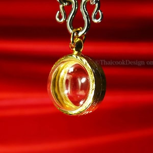 May include: A gold pendant with a clear glass insert hangs from a silver chain. The pendant is round and has a decorative border. The chain has a lobster clasp. The pendant is on a red background.