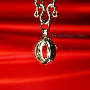May include: A silver chain necklace with a round, hollow pendant. The pendant has a smooth, reflective surface and appears to be made of metal.