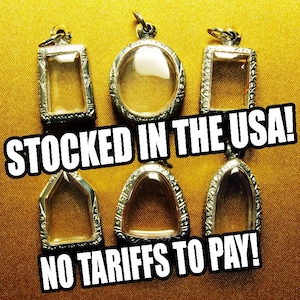 May include: Six silver-toned pendant cases with clear glass inserts, in various shapes, are displayed on a gold-colored surface. The text "STOCKED IN THE USA!" and "NO TARIFFS TO PAY!" are overlaid on the image.