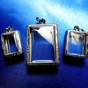 Może przedstawiać: Trzy srebrne, ozdobne, prostokątne ramki z przezroczystymi wkładkami szklanymi. Ramki są w różnych rozmiarach i wiszą na srebrnym oczku.
