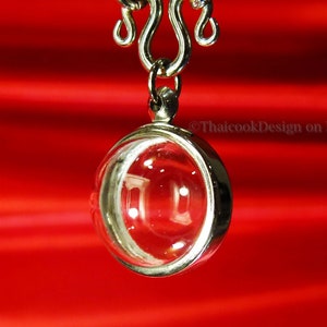 May include: A silver chain necklace with a round, clear glass pendant. The pendant is hanging against a red background.