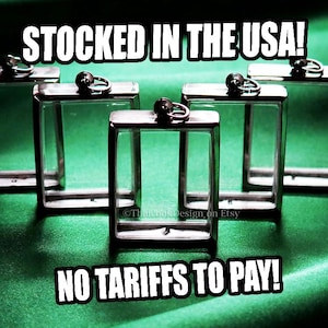 May include: Several clear, rectangular glass display cases with silver-colored metal frames are arranged on a green surface. The text "STOCKED IN THE USA!" and "NO TARIFFS TO PAY!" are displayed in white block letters.