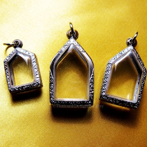 Może przedstawiać: Trzy srebrne zawieszki z przezroczystymi wkładkami szklanymi. Zawieszki mają kształt domów z ozdobnymi wzorami wokół krawędzi.