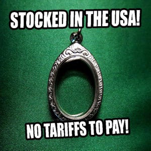 May include: A silver-colored, teardrop-shaped pendant with an ornate, swirling design around the edges. The pendant is empty in the center. The text "STOCKED IN THE USA!" and "NO TARIFFS TO PAY!" are displayed in white.