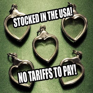 May include: Five silver-toned heart-shaped pendants with a clear center, arranged on a green textured surface. The pendants have a small loop at the top for hanging. Text in the image reads "STOCKED IN THE USA!" and "NO TARIFFS TO PAY!"