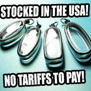 May include: Four silver-toned metal pendant frames with clear, hollow centers and attached jump rings. The text STOCKED IN THE USA! appears at the top and NO TARIFFS TO PAY! appears at the bottom of the image against a light blue background.