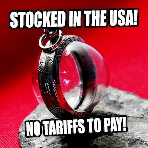 May include: A clear, round glass object with a red interior, encased in a decorative silver metal frame. The text "STOCKED IN THE USA!" and "NO TARIFFS TO PAY!" are displayed in white, bold font.