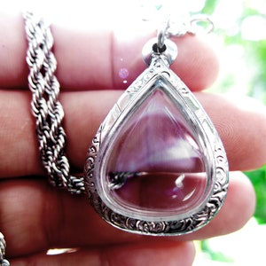 May include: A silver pendant necklace with a teardrop-shaped clear glass charm. The charm has a delicate floral design around the edge.