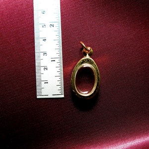 K&ouml;nnte beinhalten: Ein ovaler Anh&auml;nger aus Gold mit einem transparenten Glaseinsatz. Der Anh&auml;nger ist etwa 3,8 cm lang und hat ein filigranes Design.